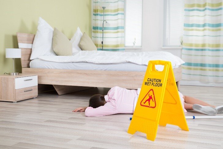 a women in a pink shirt lying on the floor in front of 'caution wet floor' warning sign